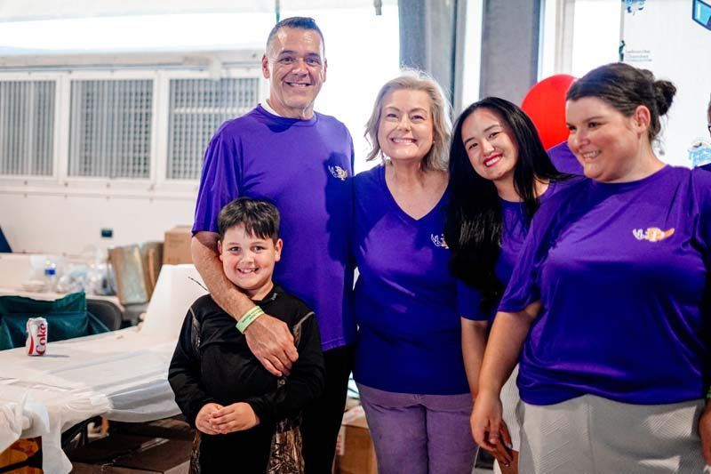 Five smiling people in purple shirts pose in a bright room with tables and chairs