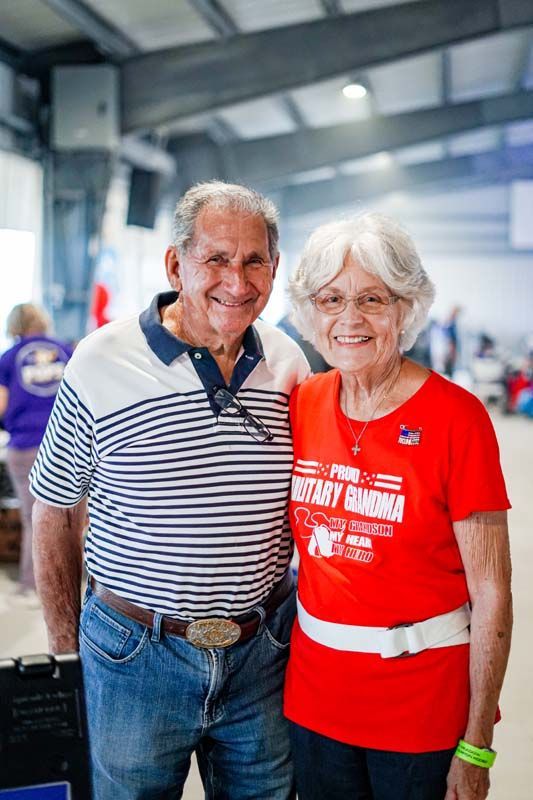 Smiling couple posing indoors, wearing striped and red shirts at an event.