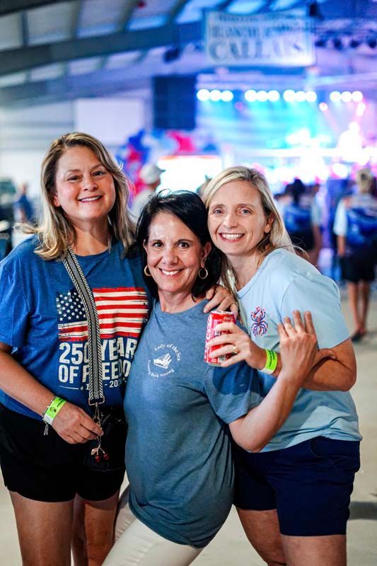 Three smiling people pose together at an indoor event, with bright stage lights behind them.