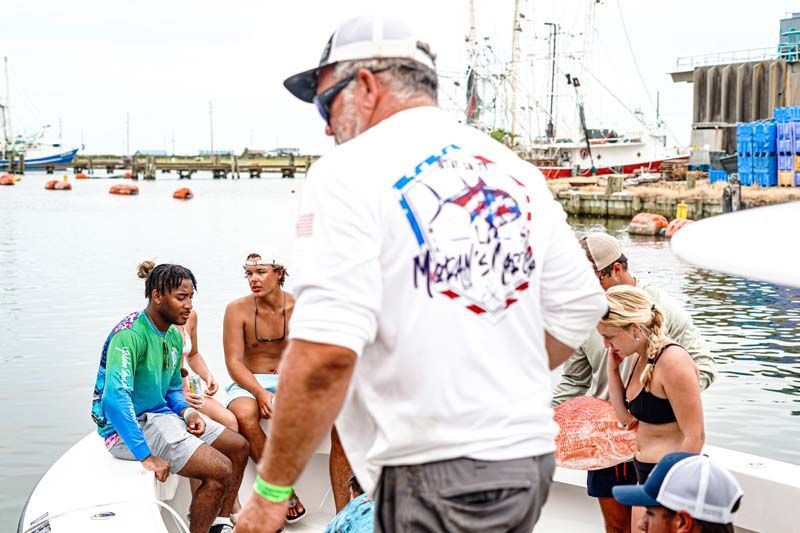 A man in a white shirt is standing on a boat with a group of people.