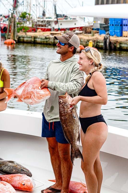 A man and a woman are standing on a boat holding fish.
