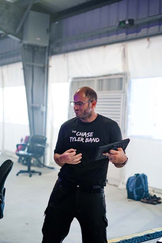Man in black shirt and pants gesturing in an industrial studio, holding a tablet.
