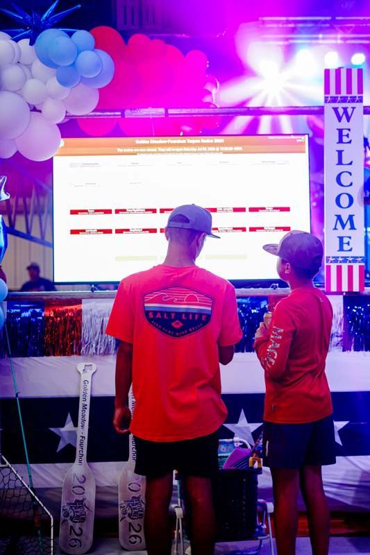 Two people in red shirts facing a bright welcome display with balloons and star decorations