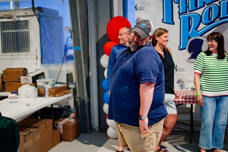 People standing in a room with red, white, and blue balloons and a large blue sign.