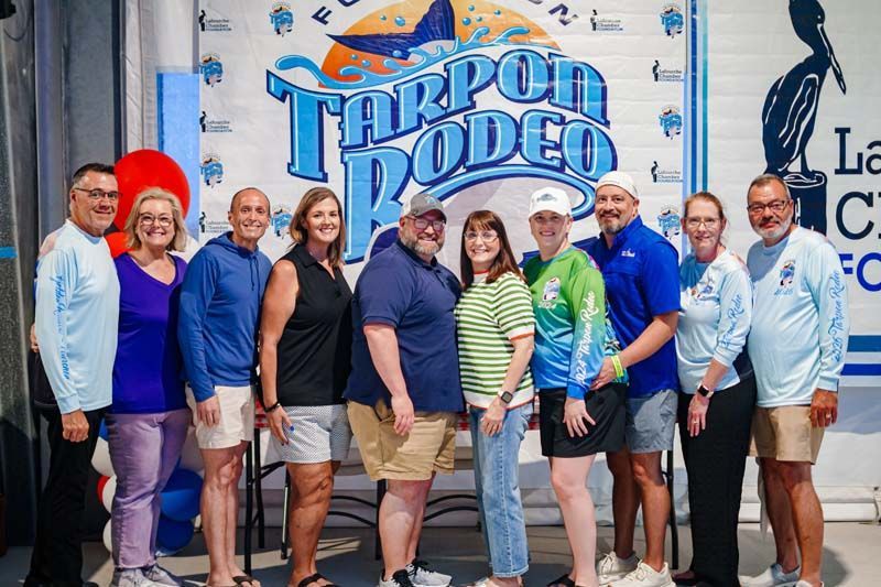 Group of people posing in front of a “Tropi Rodeo” sign at an indoor event booth