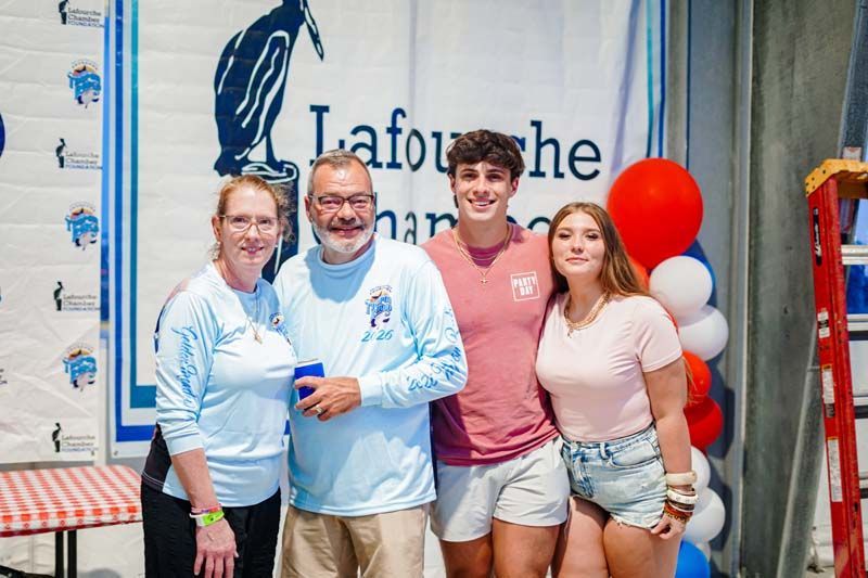 Four people posing indoors in front of a Laforche banner, with red and blue balloons nearby