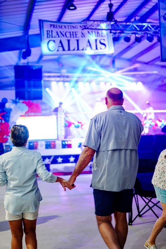 Couple holding hands under bright lights at a seaside promenade with a “Calais” sign in the background