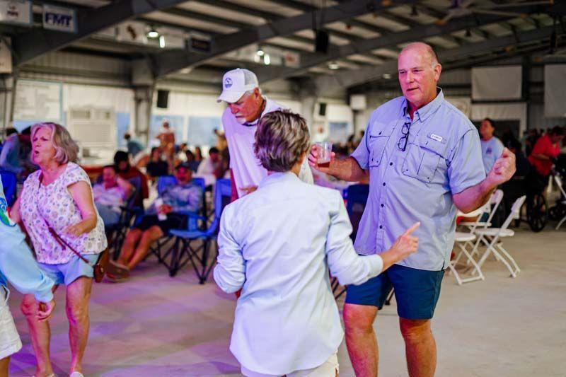 People dancing in a bright indoor hall, with a seated crowd in the background.