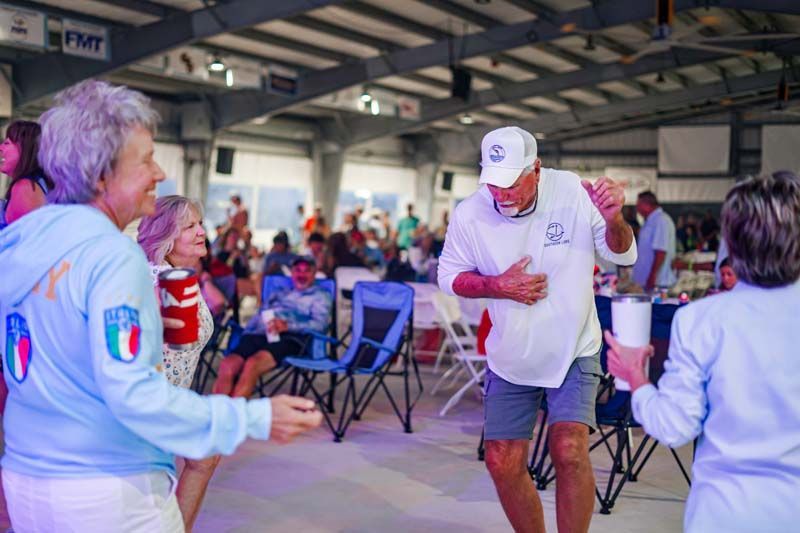 People dancing in a covered pavilion with folding chairs and spectators in the background