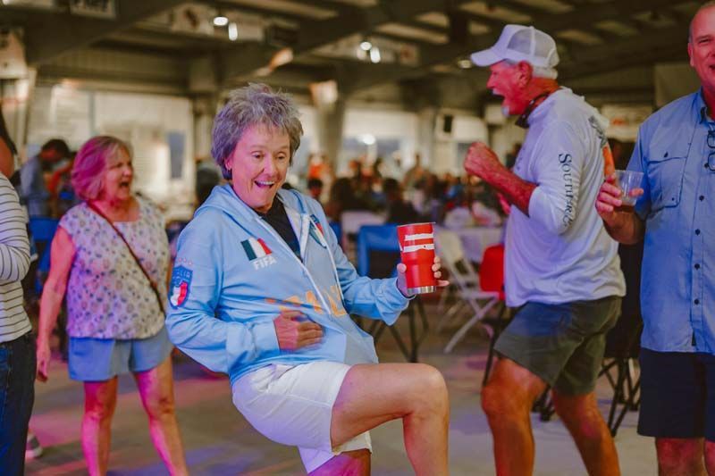 People dancing at an indoor event, smiling and holding drinks in a lively crowd