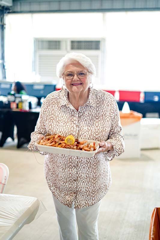 An elderly woman is holding a tray of shrimp.