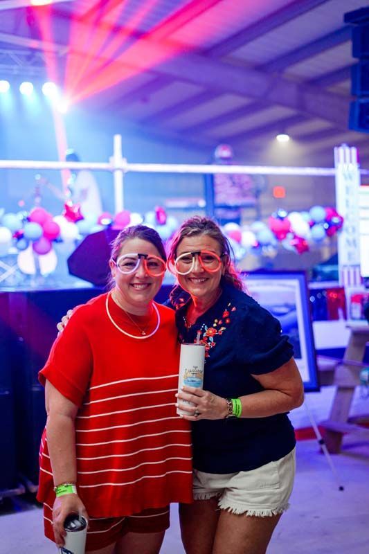 Two people smiling and posing at a colorful indoor party with balloons and bright lights