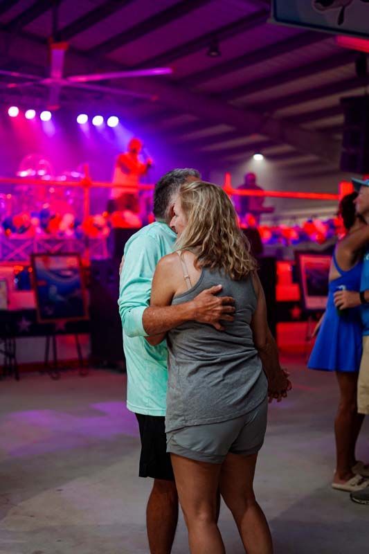 Two people embrace on a dance floor under purple stage lights at a lively event.