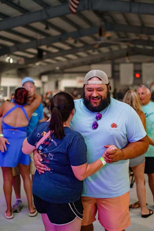 Two people dance together in a covered outdoor venue, smiling and holding hands.