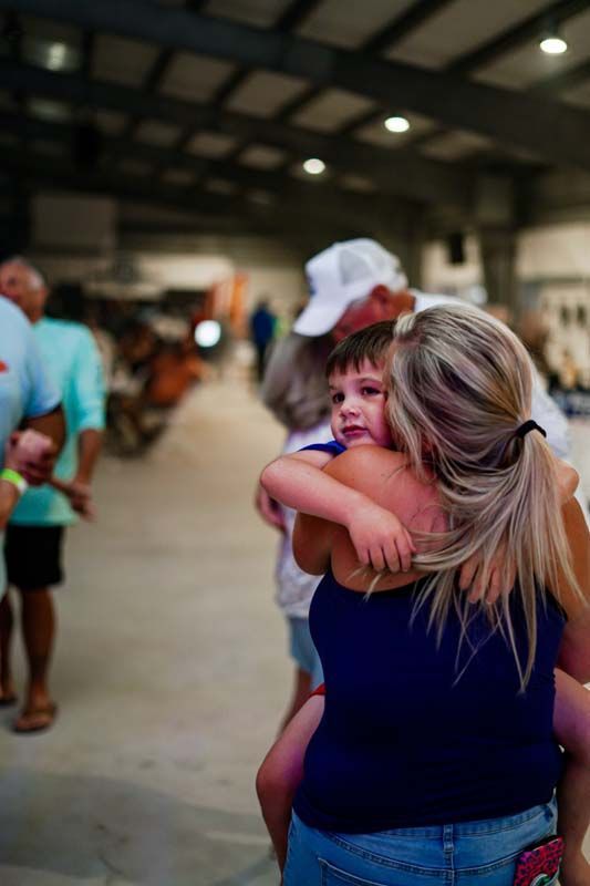 Woman holding a child in a busy indoor hall, seen from behind