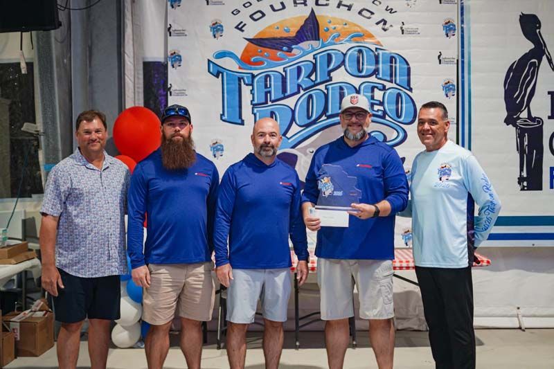 Five men posing on a stage in front of a Tarpon Rodeo banner, holding a plaque.