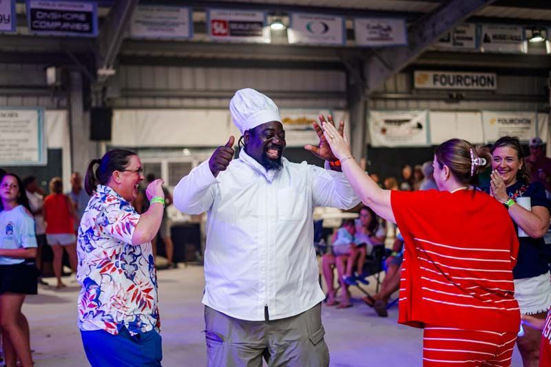 People dancing in a market hall, including a chef in white and a woman in red raising their hands.