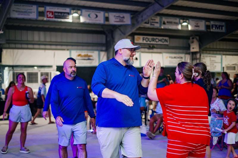 People dancing in a large indoor hall, with a man in blue and a woman in red striped shirt in front.