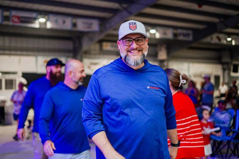 Smiling man in blue shirt and white cap standing in a crowded indoor event venue