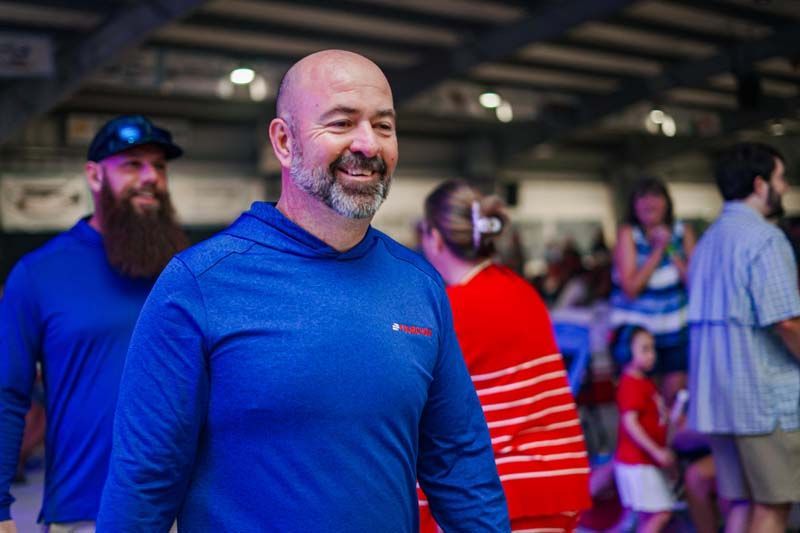 Smiling man in a blue shirt at an indoor event, with people blurred in the background