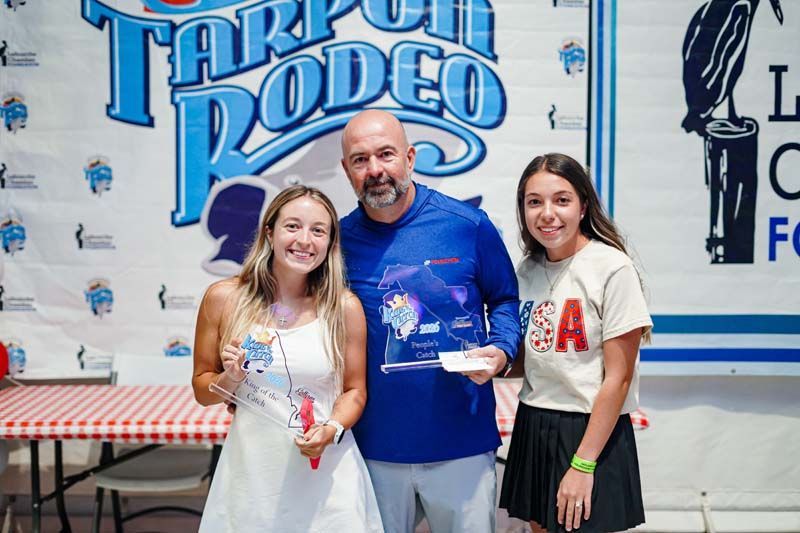 Three people posing with trophies at the Tarpon Rodeo award booth.