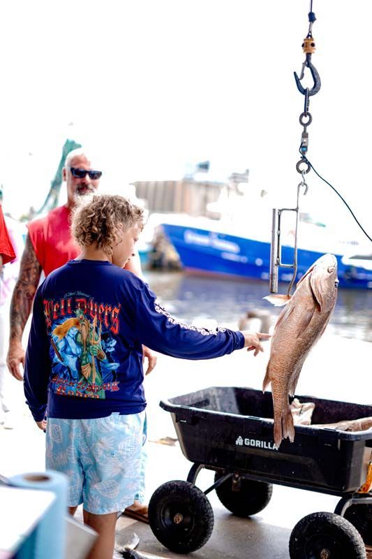 Person hoists a large fish over a wheeled tub at a dockside fish-cleaning station
