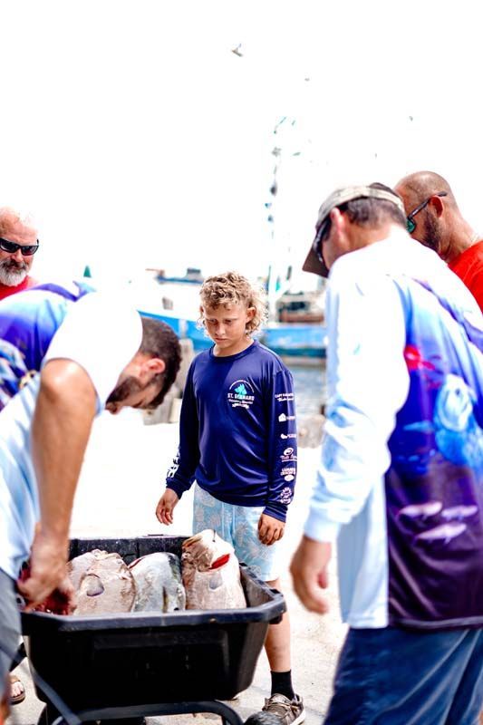 People in blue shirts surrounding a wheelbarrow of fish at an outdoor event