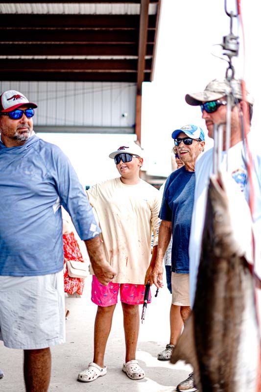 People standing on a dock beside fishing gear, wearing sunglasses and casual clothes.