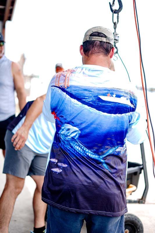 Person seen from behind in a blue shirt holding a hook on a boat deck