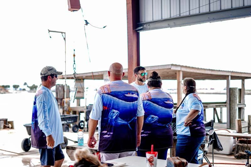 People in blue shirts standing on a dock beside a boat, with one person wearing a mask