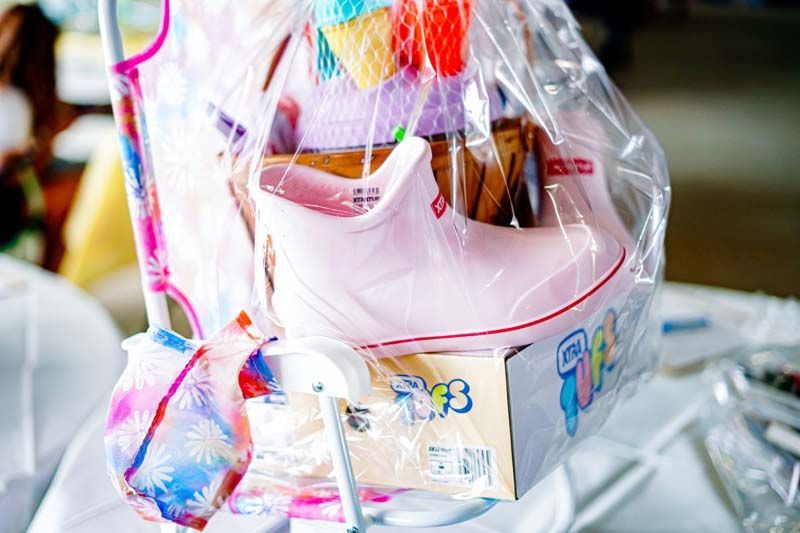 A pink-and-white baby carrier wrapped in clear plastic, sitting among colorful items on a table.