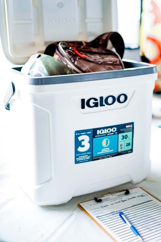 White Igloo cooler open on a table with bags and ice packs inside, next to a clipboard.