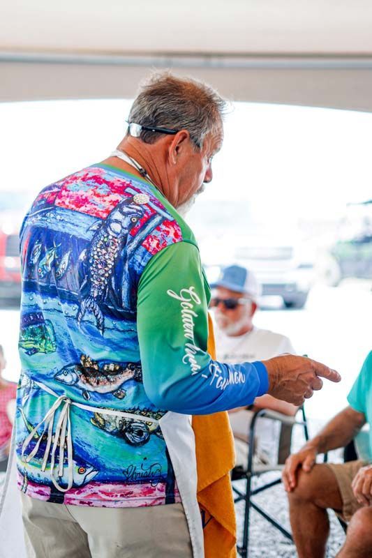 Man in a colorful fishing shirt on a boat points while holding a drink