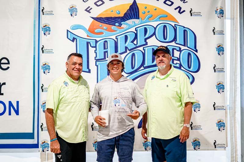 Three men are standing in front of a tarpon rodeo sign.