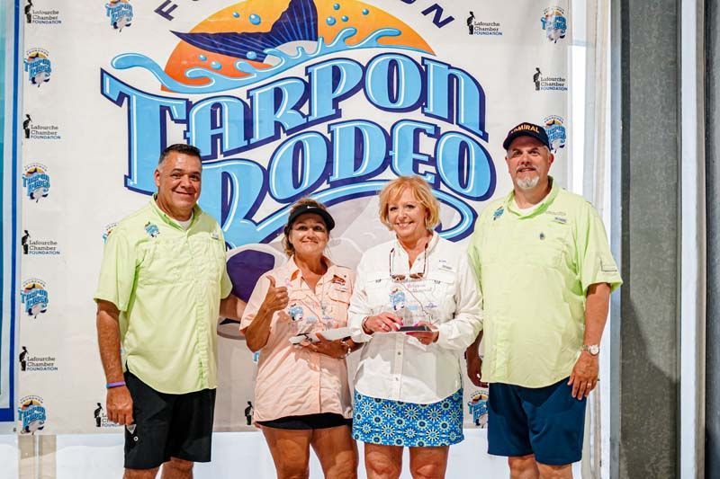 A group of people standing in front of a tarpon rodeo sign.
