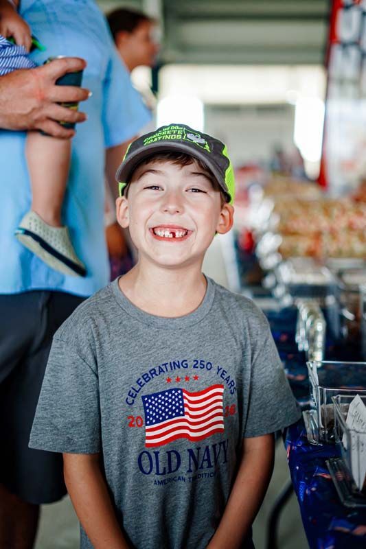 Smiling child in a gray Old Navy shirt and cap, standing in a busy indoor market.