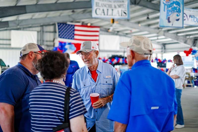 People chatting at an indoor rally under American flags, one holding a red cup
