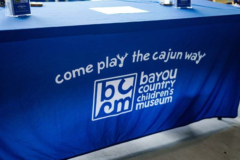 Blue tablecloth with Bayou Country Children's Museum logo and slogan, “Come play the cajun way.”