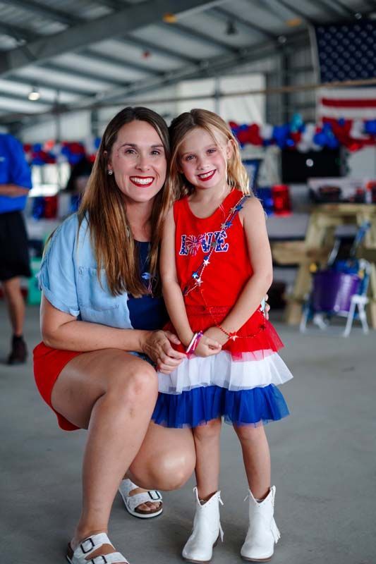 Woman and young girl in red, white, and blue outfits posing indoors with patriotic decorations
