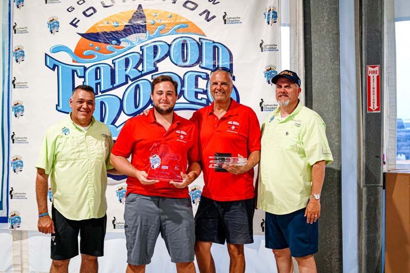 A group of men are posing for a picture in front of a tarpon dodge sign.