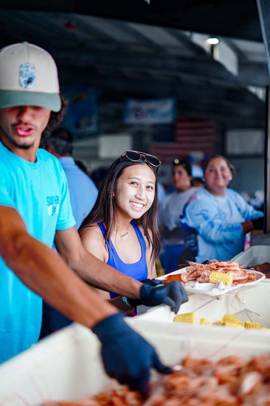 Volunteers in gloves serve food at a buffet line indoors.