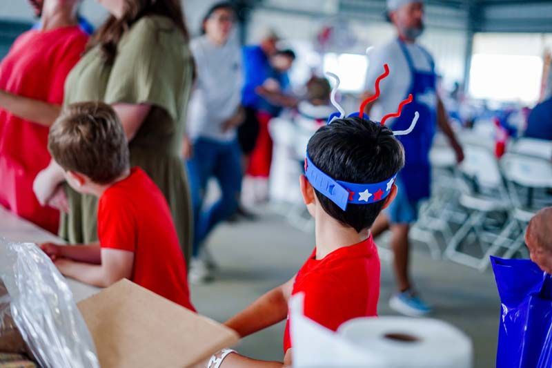 Child in red shirt and blue star-spangled headband at a crowded indoor event