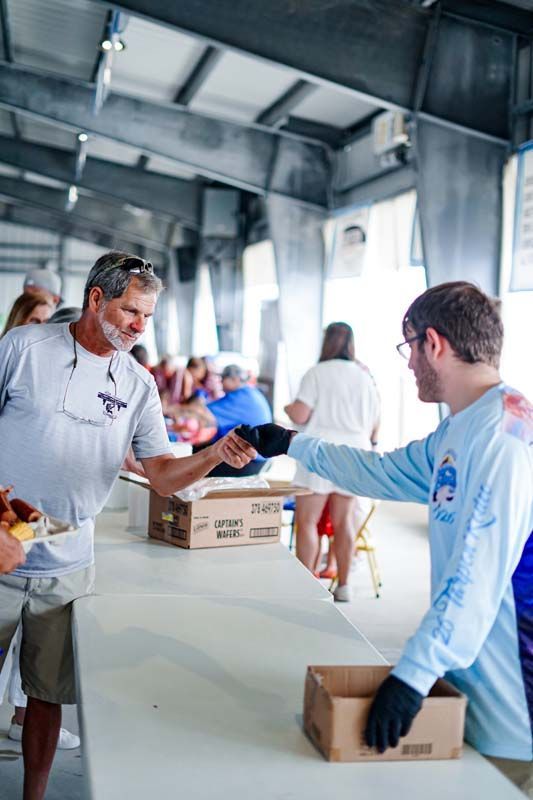 People in light blue shirts packing and handing boxes at a donation table indoors