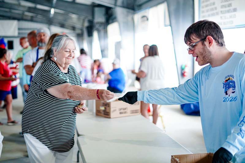 Volunteer handing a snack to a smiling attendee at a community event table