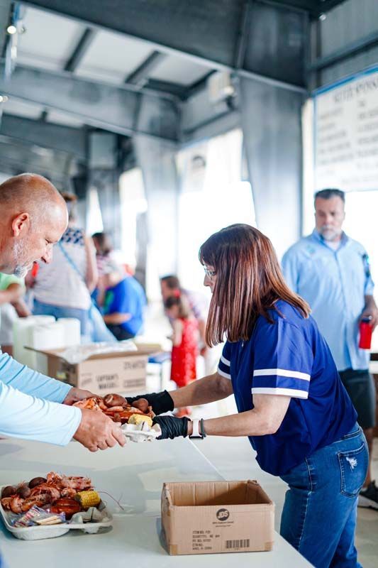 Volunteer handing food to a recipient at a donation table in a busy indoor setting