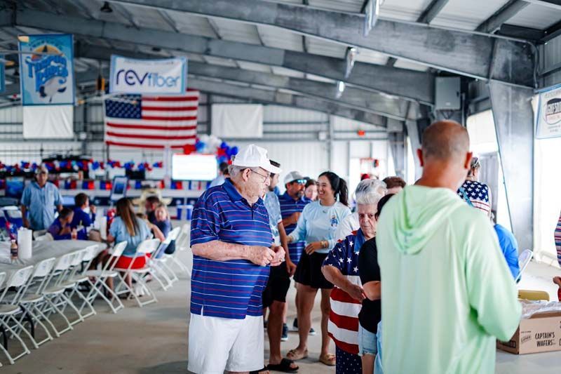 People gathered in a pavilion with American flags and folding chairs at a community event.