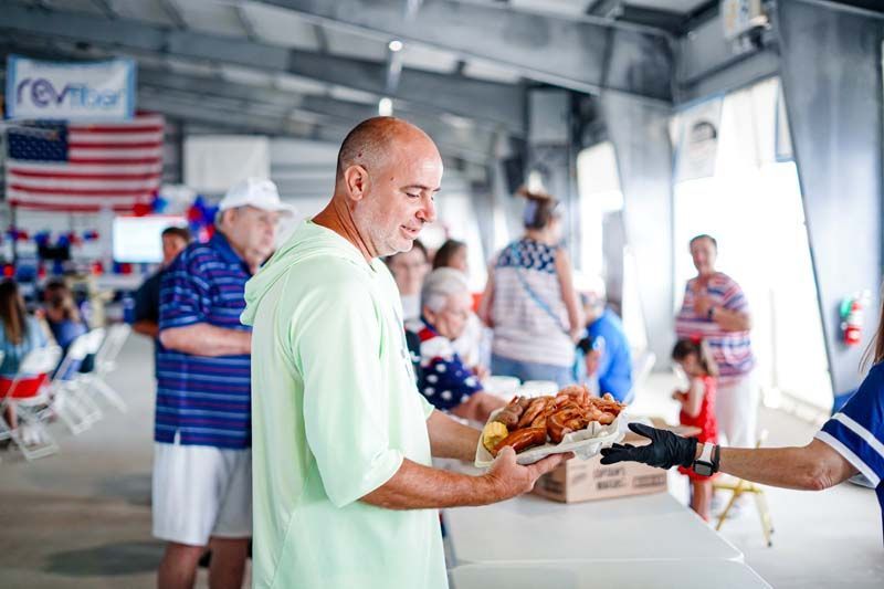 Man in light green shirt receives food at a busy indoor counter with people and an American flag in the background
