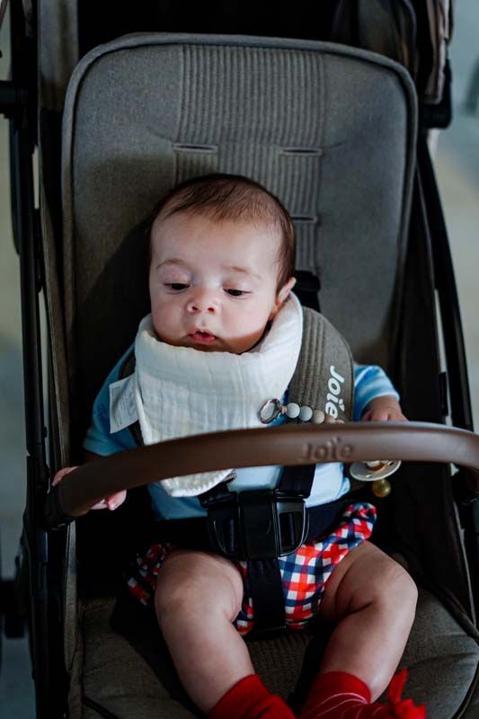 Baby seated in a stroller, wearing a bib and blue shirt, looking down with a neutral expression.