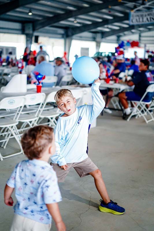 Children playing with a blue balloon in a pavilion with tables and chairs