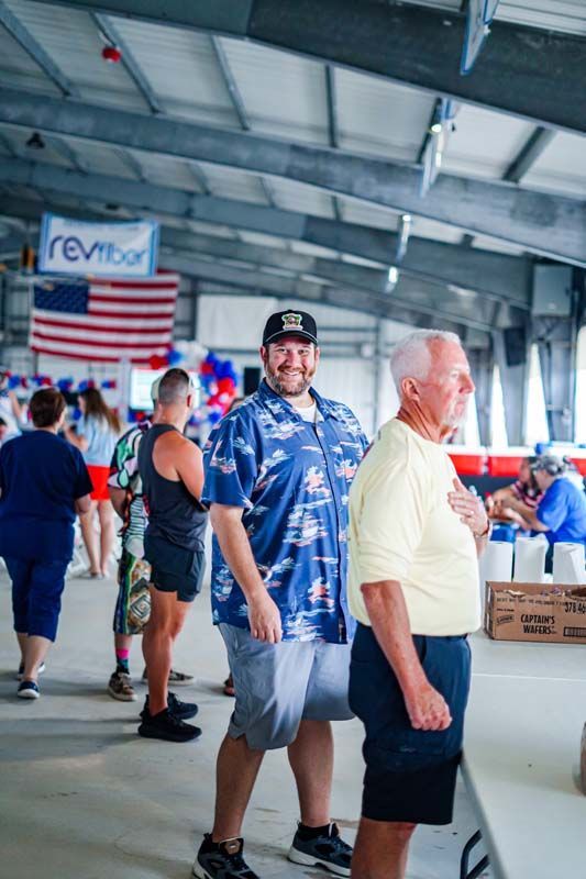 People standing in a stadium concourse near an American flag banner and vendor table.